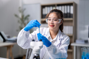 A woman in a lab coat is holding a test tube and wearing blue gloves