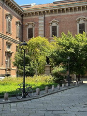 Obraz premium Charming courtyard with a bicycle parked under a classic streetlamp, surrounded by lush greenery and historical architecture. Milan, Italy 