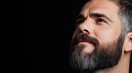 Obraz premium Portrait of a handsome man with a well-groomed beard looking thoughtfully into the distance against a dark background
