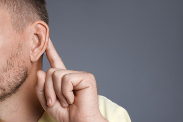 Man showing hand to ear gesture on grey background, closeup. Space for text