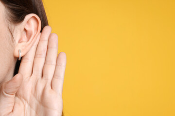 Woman showing hand to ear gesture on orange background, closeup. Space for text