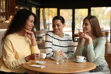 Happy women with coffee drinks chatting in cafe