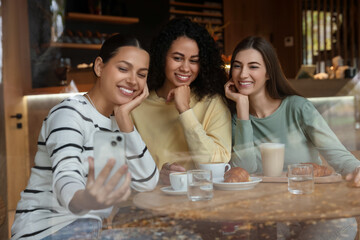 Women taking selfie at coffee meeting in cafe, view through window
