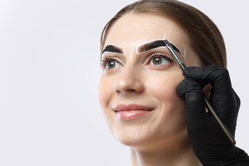 Young woman undergoing henna eyebrows dyeing on light background, closeup. Space for text