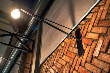 A sleek industrial-style wall lamp mounted against a rustic herringbone brick wall. The combination of modern lighting and exposed brick creates a contemporary, cozy atmosphere