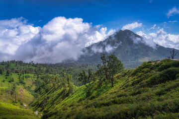 In this stunning mountainous area, lush greenery blends with dynamic clouds under a bright blue...