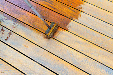 Close-up of a wooden deck being stained with a brush for protection and maintenance during a home...