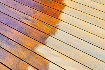 Close-up of a wooden deck showing the process of restoration with a half-stained surface...