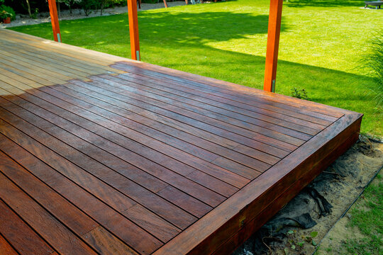 Close-up of a wooden deck - on the covered terrace - showing the process of restoration with a half-stained surface contrasting weathered and treated wood during a home improvement project 