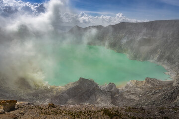 A stunning aerial vista showcasing a magnificent Ijen volcano, burning sulfur deposit releasing steam, framed by azure waters of acid lake under the radiant sunlight, East Java, Indonesia