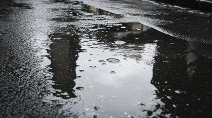 Obraz premium Rainwater puddle reflects distorted building shapes on asphalt