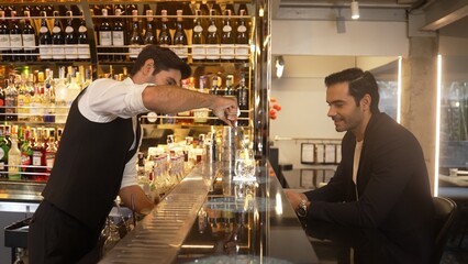 Smart bartender serving drink gin fizz with lemon sliced to VIP guest while waiting friend at luxurious counter bar. Barman providing excellent service at vibrant nightlife party atmosphere. Vinosity.