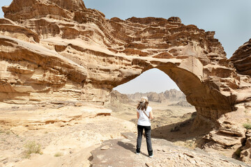 Tourist admiring the imposing natural arch rock formation in Hisma valley desert, Saudi Arabia