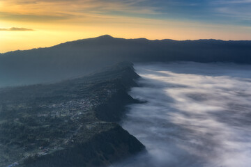 An aweinspiring aerial view reveals mist gracefully enveloping majestic Bromo mountains at sunrise, showcasing natures serene beauty and creating a tranquil atmosphere, East Java, Indonesia