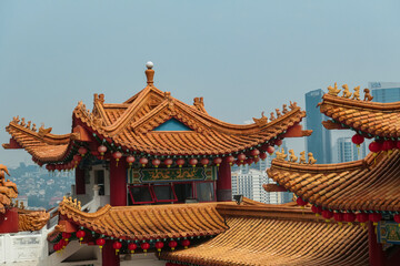 Fototapeta premium Iconic architecture of Chinese Thean Hou Temple. Roof is adorned with vibrant colors, intricate patterns, decorative figures. Rows of red lanterns. Cityscape of Kuala Lumpur, Malaysia, Southeast Asia