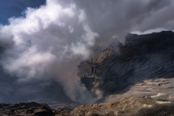 The breathtaking view of a Bromo volcanic crater, surrounded by swirling steam and billowing smoke,...