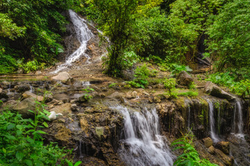 A breathtaking Tumpak Sewu Waterfall cascades down rocky cliffs, surrounded by lush greenery, creating an idyllic setting for relaxation and inspiration in nature, East Java, Indonesia