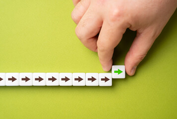 A hand makes a path out of blocks with arrows. The concept of moving forward and continuing progress. Strategic planning, forward momentum, and the continual pursuit of growth and improvement © Andrii Yalanskyi