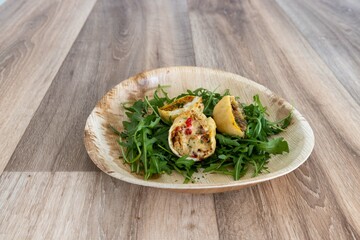 A visually appealing and appetizing dish, featuring crispy, golden-brown stuffed pastries resting on a bed of fresh arugula, served on a sustainable palm leaf plate.