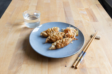 A visually appealing and appetizing plate of pan-fried gyoza dumplings served on a gray plate, accompanied by a side of fresh slaw and a glass of water. Chopsticks are placed beside the plate