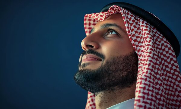 Zoom in to Saudi man looking up with proud and smile, wearing saudi arabian attire presentable and sharp, solid blue navy background, emotional with grain effect