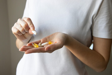 Obraz premium Сlose-up of a woman's hands with various pills and supplements. Woman taking omega 3, omega 6, omega 9, fish oil capsules, vitamin D and vitamins. Vitamins for women.