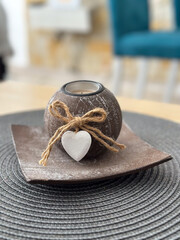 Rustic candle holder with a wooden heart accent sitting on a table. The piece embodies warmth,...