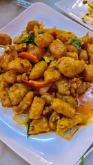 Serving of sweet and sour chicken.hicken pieces are coated in a golden-orange sauce and interspersed with vegetables, onions, carrots, and perhaps some peppers. The dish looks glossy and appetizing