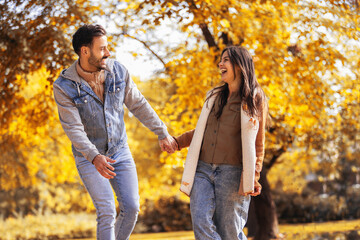 Fototapeta premium Young happy couple holds hands and runs in the colorful park on a sunny autumn day.