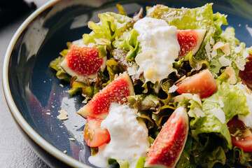Fresh fig and burrata salad with leafy greens, almonds, and creamy dressing in a rustic blue bowl