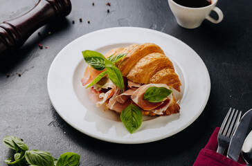 Fresh croissant sandwich with prosciutto and basil served on plate, perfect for a gourmet breakfast