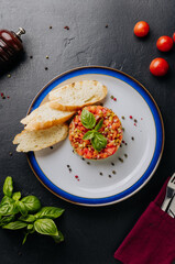 Guacamole tartare with fresh vegetables, basil garnish, and crispy baguette slices on a white plate