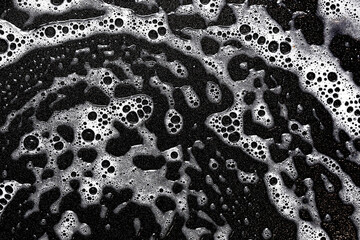 Foam texture. White bubbles on a black background. Washing a frying pan. Soapy texture. Cleaning process backdrop. Smudges of water with detergent.