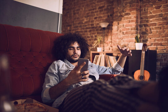 Man relaxing on couch with headphones and a smartphone in bar
