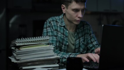 Focused and concentrated guy student e learning online on internet website. Young man working remotely at home office desk, makes notes in work document, looks at laptop computer
