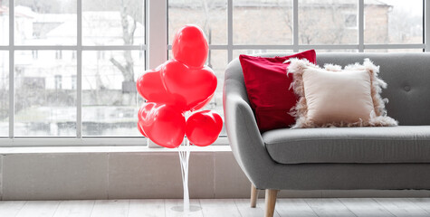 Interior of living room with grey sofa and heart-shaped balloons near window. Valentine's Day...