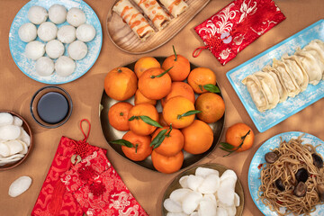 Chinese New Year food arrangement on a table, featuring dumplings, noodles, oranges with red envelopes for gifts