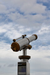Vintage aluminum and bronze coin-operated public telescope pointing to the mostly cloudy with blue patches sky over Saint-Malo. Brittany-France-198