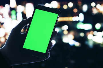 Hand holding smartphone with green screen in night city lights background