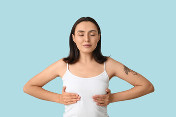 Young woman checking her breast on blue background. Cancer awareness concept