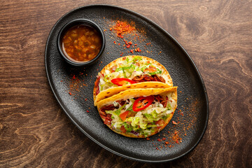 Delicious taco platter featuring a soft and crispy taco filled with fresh lettuce, diced tomatoes, and spices, served with a side of savory salsa. Perfect for food lovers.