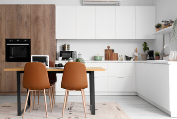 Wooden table with laptop, tea set and notebook in interior of modern kitchen
