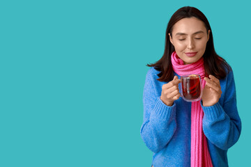 Beautiful young woman in scarf with glass cup of hot mulled wine on blue background