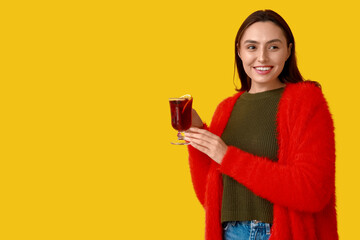 Happy young woman with glass cup of hot mulled wine on yellow background