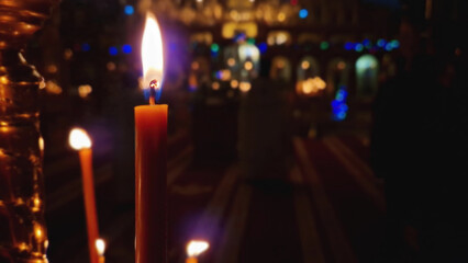 Closeup of a lit candle on the candlestick inside a Christian Orthodox church. The burning flame is sharp and bright. Religious symbol for Easter or Christmas holidays. Religion and creed concept