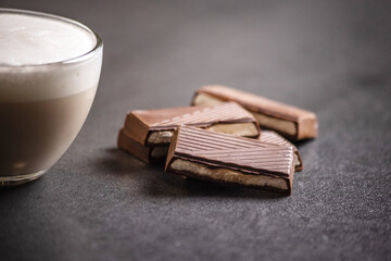 a cup of delicious, aromatic coffee with foam and pieces of dark chocolate on a dark background.