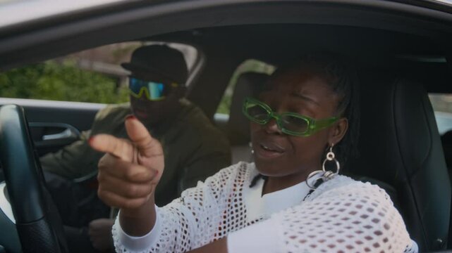 Handheld close-up shot of cool Black lady in glasses and classy hip-hop outfit sitting in white modern car with boyfriend and rapping to camera, recording music video