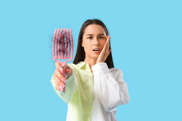 Shocked young woman with hair loss problem on blue  background
