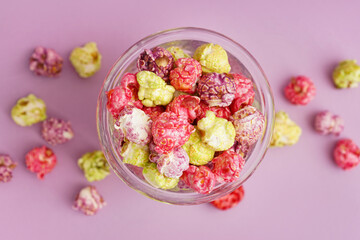Glass with sweet colorful popcorn on lilac background