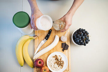 Woman hands pouring a protein drink, milkshake, or smoothie from a shaker into a glass in her hand, in the kitchen, top view